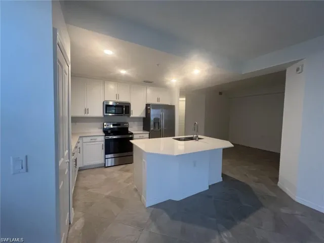 Kitchen with stainless steel appliances, white cabinetry, an island with sink, recessed lighting, and light stone countertops