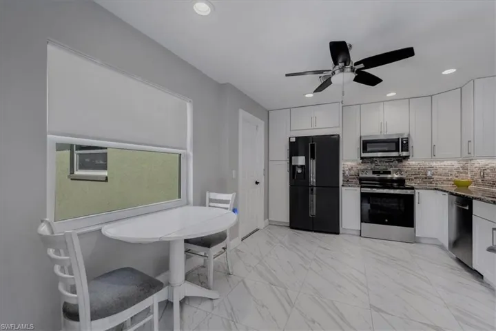Kitchen featuring appliances with stainless steel finishes, light marble finish flooring, white cabinets, dark stone counters, and ceiling fan