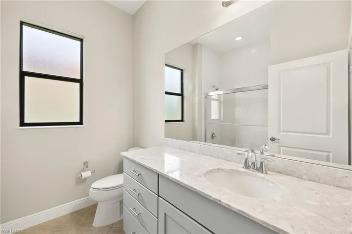 Bathroom with a wealth of natural light, tile patterned floors, baseboards, and a shower with door