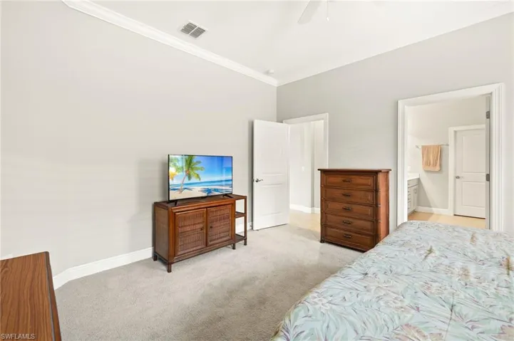 Carpeted bedroom with ceiling fan, baseboards, crown molding, and visible vents