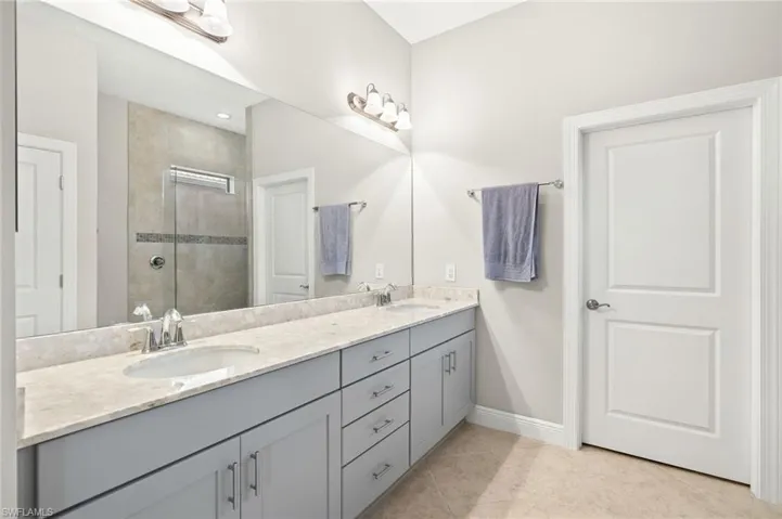 Full bathroom featuring baseboards, double vanity, tiled shower, and a sink
