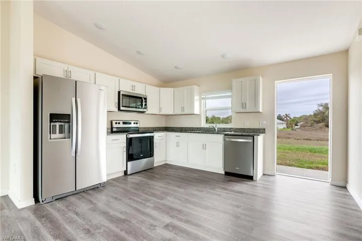 Kitchen with stainless steel appliances, lofted ceiling, white cabinets, and light wood finished floors