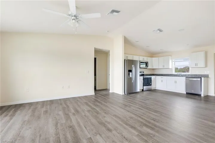 Kitchen featuring stainless steel appliances, open floor plan, dark wood finished floors, a ceiling fan, and white cabinetry