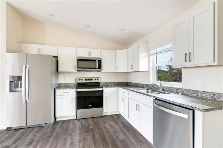 Kitchen featuring stainless steel appliances, white cabinets, dark wood-type flooring, vaulted ceiling, and dark stone counters