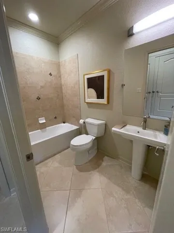 Bathroom with tile floors, tiled shower / bath, crown molding, and toilet