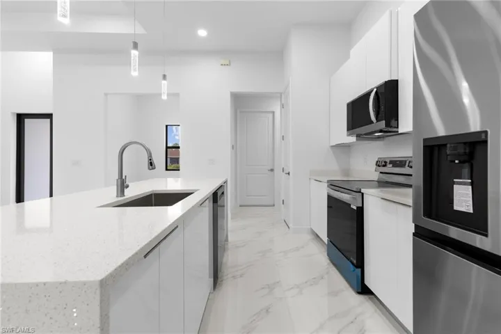 Kitchen featuring decorative light fixtures, appliances with stainless steel finishes, and white cabinets