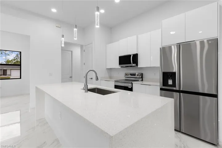 Kitchen with stainless steel appliances, hanging light fixtures, sink, and a kitchen island with sink