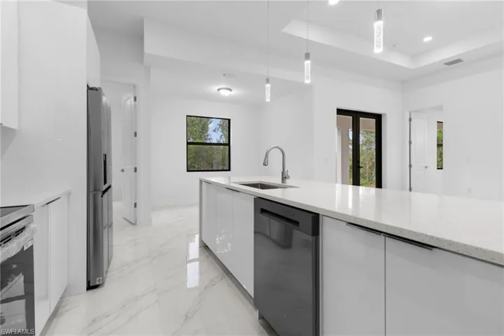Kitchen featuring dishwashing machine, plenty of natural light, a raised ceiling, and light stone countertops