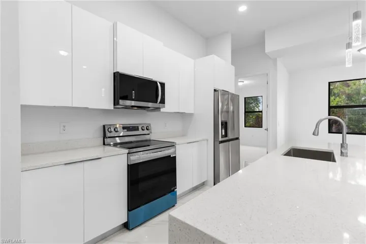 Kitchen featuring light stone counters, hanging light fixtures, white cabinetry, appliances with stainless steel finishes, and sink