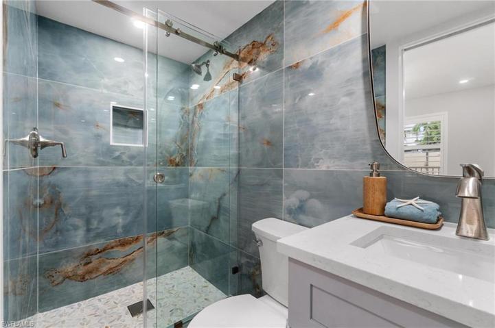 Second full bathroom is an ensuite to 2nd bedroom with large format marvel look full wall tile and custom designer quartz vanity with modern asymmetrical mirror.