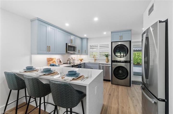 Custom grey/blue coastal cabinetry and champagne hardware with chic quartz waterfall peninsula, stainless appliance package and in unit laundry.