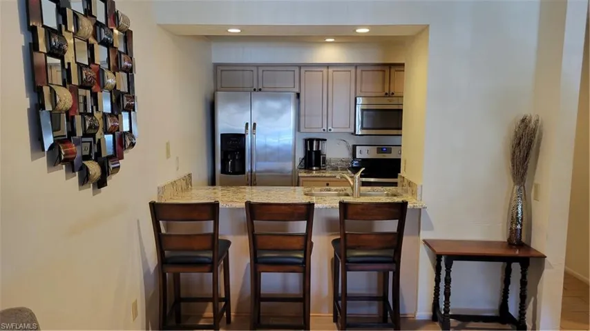 Kitchen with appliances with stainless steel finishes, a kitchen bar, light stone counters, and sink