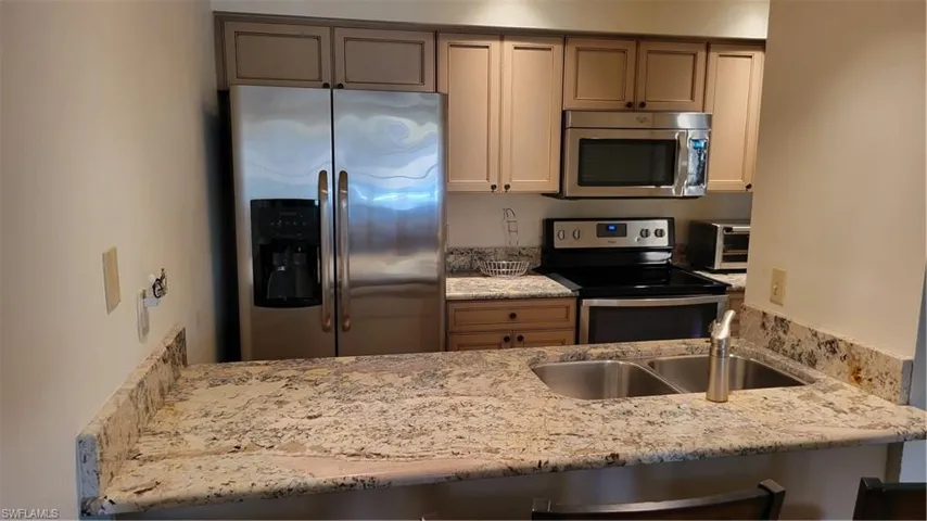 Kitchen featuring kitchen peninsula, appliances with stainless steel finishes, light stone counters, and sink