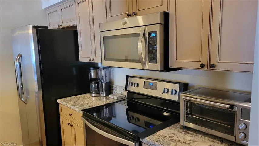 Kitchen featuring light stone counters, stove, and fridge