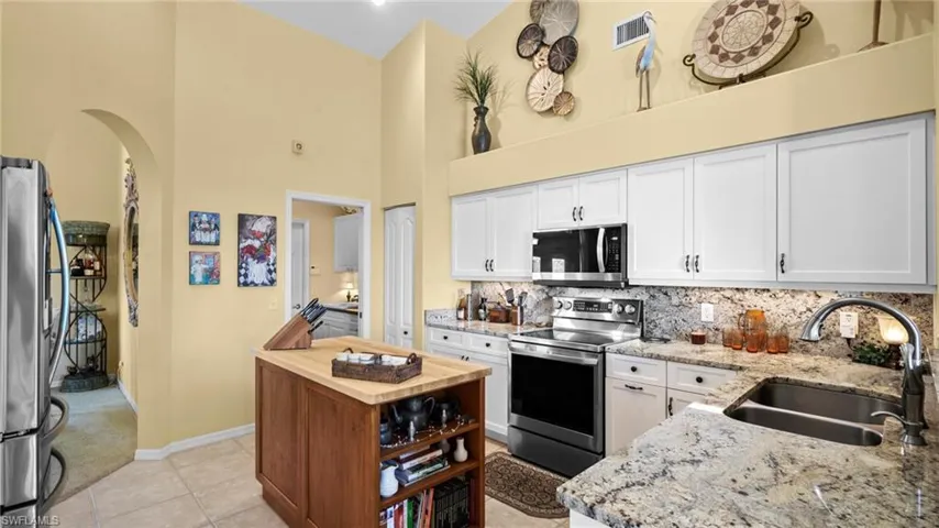 Kitchen featuring light stone countertops, sink, stainless steel appliances, a high ceiling, and white cabinets