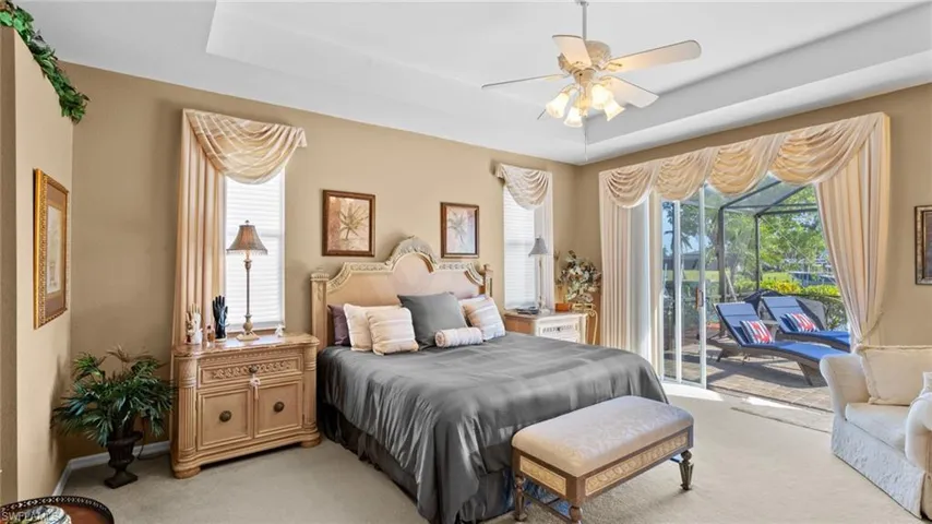 Carpeted bedroom with ceiling fan, access to exterior, and a tray ceiling