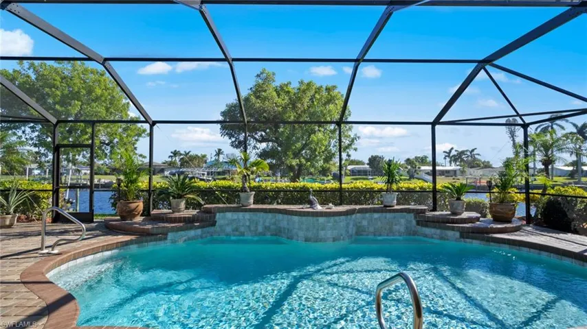 View of pool featuring glass enclosure, a water view, and a patio