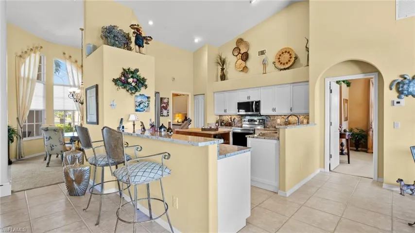 Kitchen featuring kitchen peninsula, white cabinets, stainless steel appliances, and high vaulted ceiling
