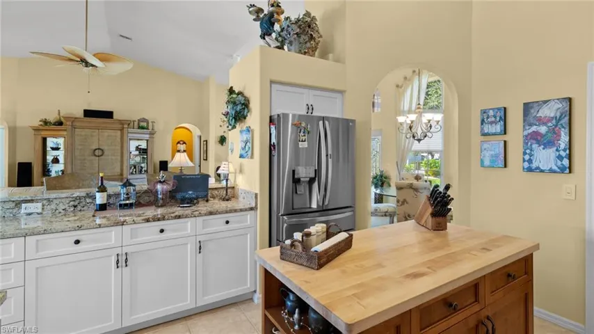 Kitchen with white cabinetry, light stone countertops, high vaulted ceiling, stainless steel refrigerator with ice dispenser, and ceiling fan with notable chandelier