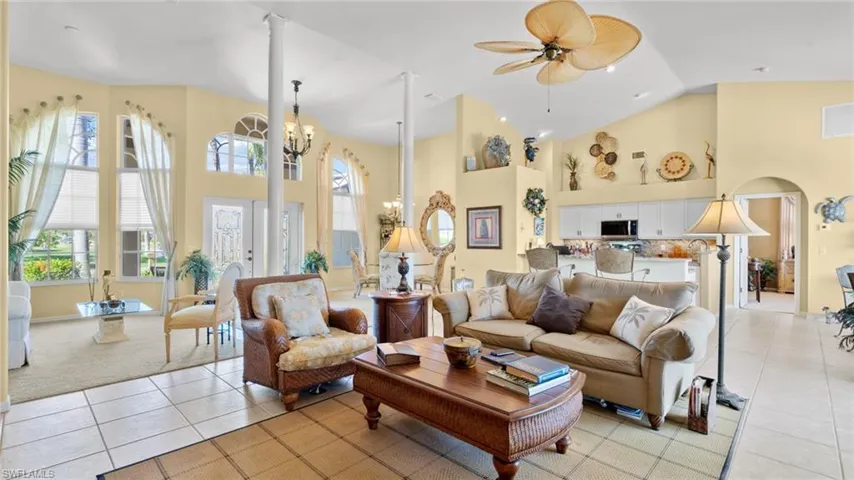 Living room featuring light tile patterned floors, ceiling fan with notable chandelier, and high vaulted ceiling