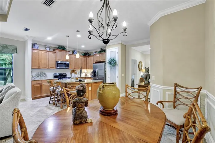 Dining space with suspended lighting, a decorative wall, crown molding, and wainscoting