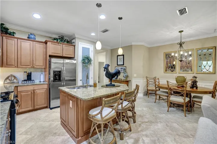 Kitchen featuring crown molding, stainless steel refrigerator with ice dispenser, light stone counters, range with gas cooktop, and a breakfast bar area