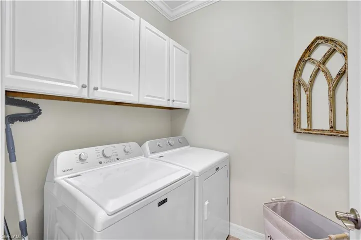 Laundry room featuring cabinet space, washing machine and clothes dryer, and ornamental molding