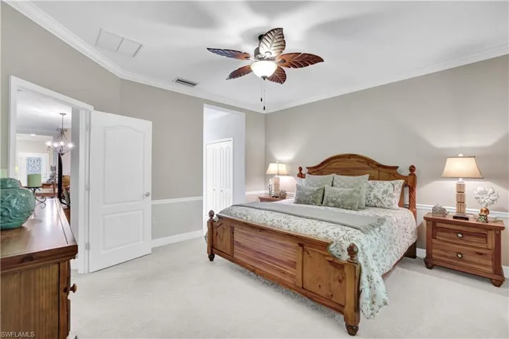 Bedroom with ornamental molding, light carpet, a ceiling fan, a closet, and a chandelier