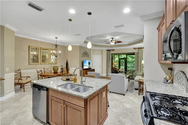 Kitchen with open floor plan, light stone counters, stainless steel appliances, a center island with sink, and crown molding