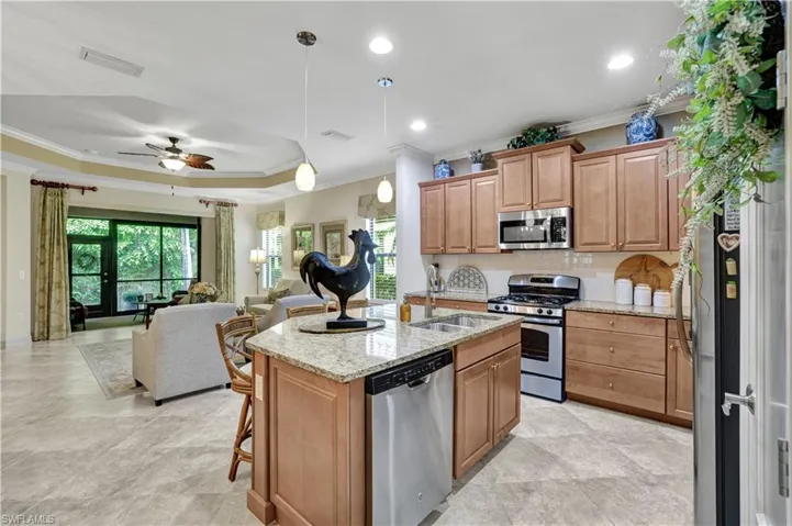 Kitchen featuring open floor plan, stainless steel appliances, light stone counters, a ceiling fan, and crown molding