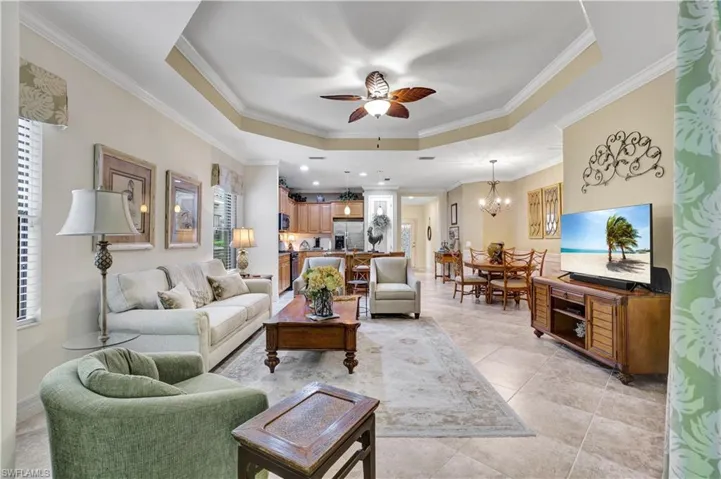 Living area with a tray ceiling, ceiling fan, hanging lights, and ornamental molding