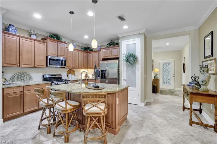 Kitchen with stainless steel appliances, light stone countertops, wood finish cabinets, ornamental molding, and a breakfast bar area