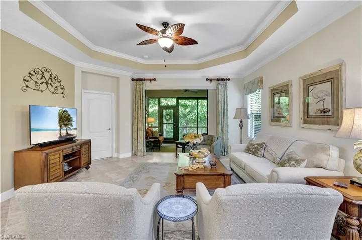 Living room featuring a ceiling fan, a raised ceiling, crown molding, and light tile patterned floors