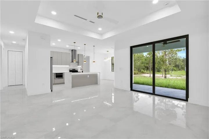 Unfurnished living room with a tray ceiling, ceiling fan, recessed lighting, and light marble finish floors