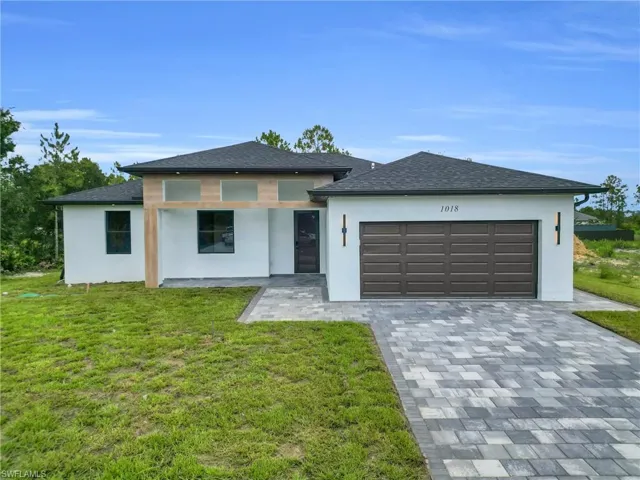 Prairie-style house featuring stucco siding, decorative driveway, a front lawn, and an attached garage