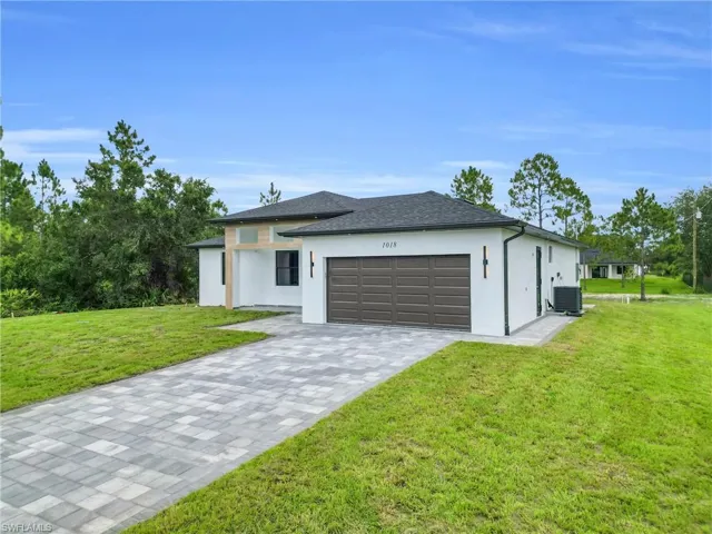 View of front of house with stucco siding, a front yard, decorative driveway, an attached garage, and a shingled roof