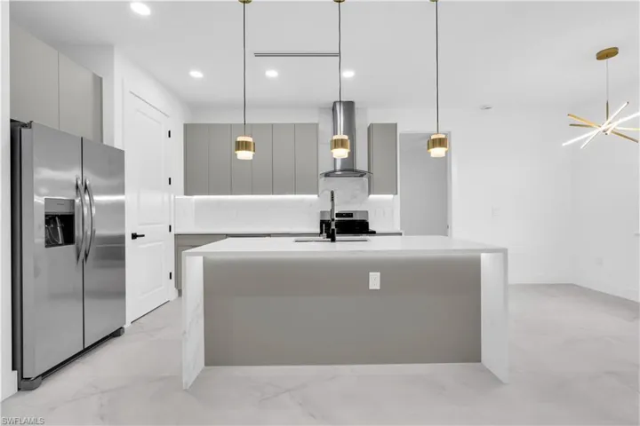 Kitchen with gray cabinetry, stainless steel appliances, an island with sink, and light stone counters