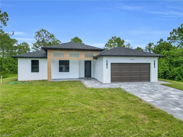 Prairie-style home with stucco siding, a front lawn, and decorative driveway
