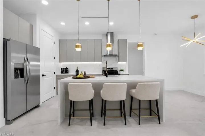 Kitchen featuring gray cabinets, stainless steel appliances, pendant lighting, an island with sink, and light stone countertops