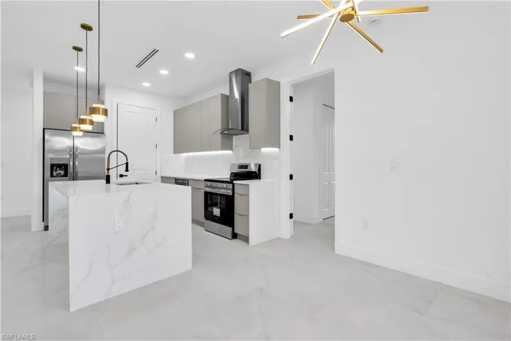 Kitchen with stainless steel appliances, decorative light fixtures, light stone counters, a center island with sink, and modern cabinets