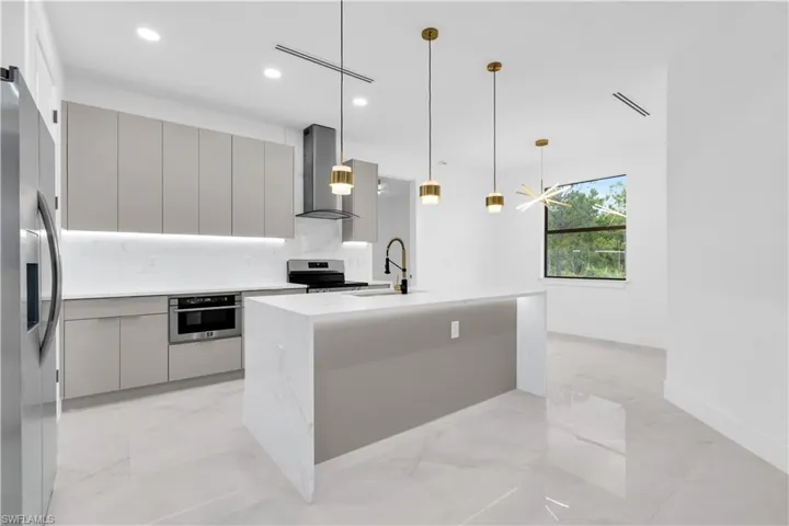 Kitchen with light stone counters, modern cabinets, a center island with sink, stainless steel appliances, and light marble finish flooring
