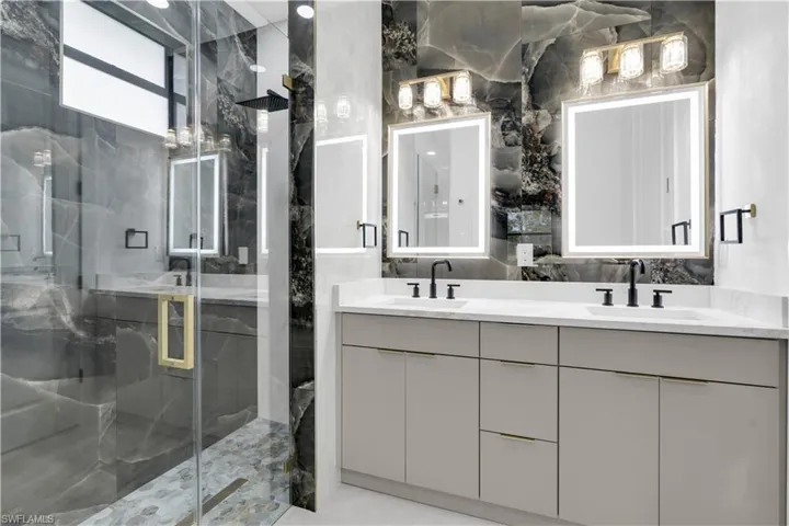 Full bathroom featuring double vanity, a marble finish shower, stone wall, and tile walls
