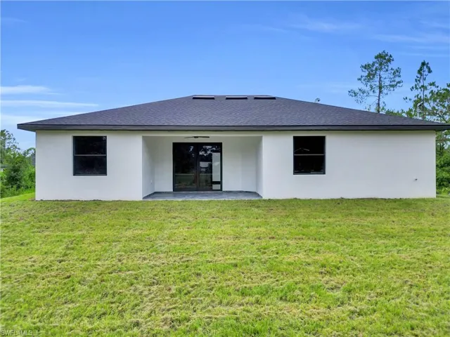 Back of house featuring stucco siding, a patio area, a lawn, and roof with shingles