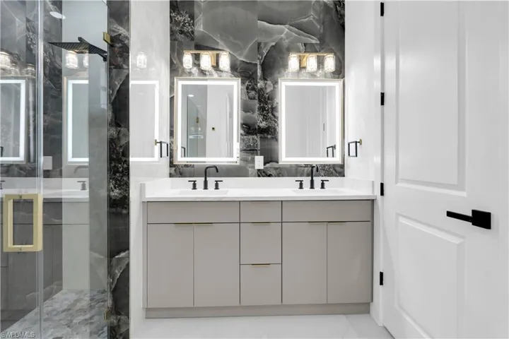 Full bathroom featuring double vanity, a marble finish shower, and tile walls