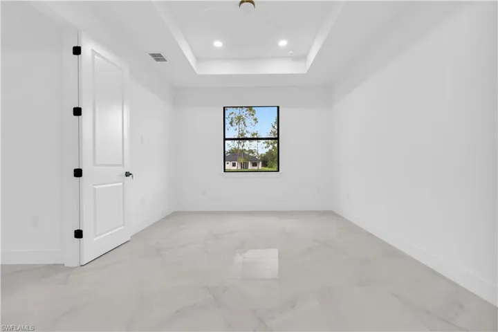 Empty room featuring recessed lighting, a tray ceiling, and light marble finish floors
