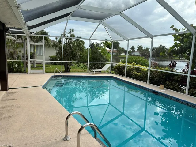 Screened outdoor pool with concrete decking, pool entry handrails, and surrounding mature landscaping