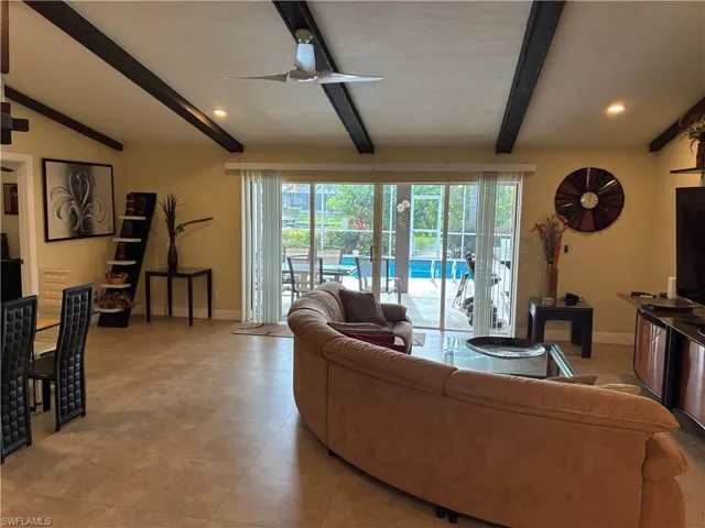 Open-concept living area with vaulted ceilings featuring exposed dark wood beams and recessed lighting