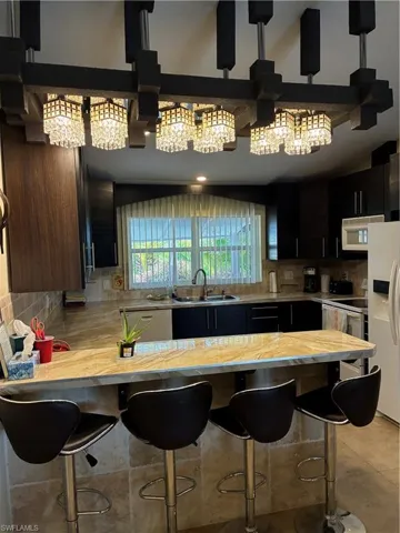 Kitchen featuring a multi-light crystal chandelier, wood-finish cabinetry, light-toned countertop, and a tiled backsplash