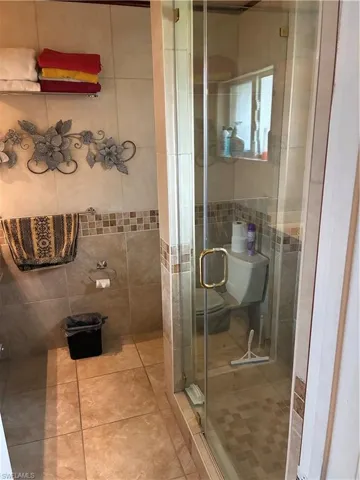 Enclosed glass shower stall with a gold-tone handle, neutral tile flooring, and coordinating wall tiles featuring a decorative mosaic band