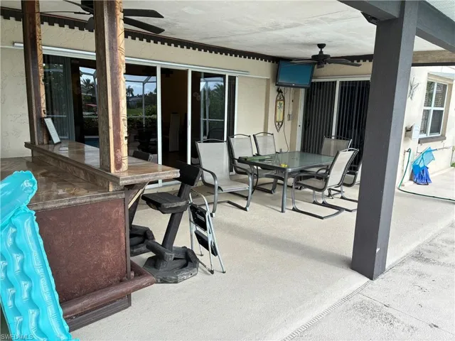 Expansive covered patio featuring a built-in bar with a stone-finish countertop, a ceiling fan, and sliding glass doors